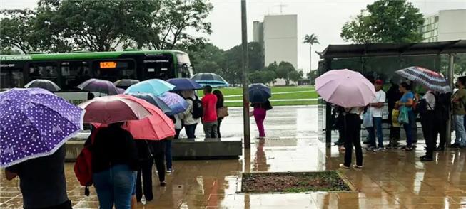 Sob chuva, pessoas aguardam ônibus em Brasília